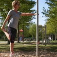 Generationenpark Frau dehnt sich im Grünen an einem Fitnessgerät; im Hintergrund Parkausstattung und blauer Himmel.