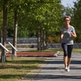 Eine Frau joggt auf einem von Bäumen gesäumten Weg im Generationenpark bei sonnigem Wetter.