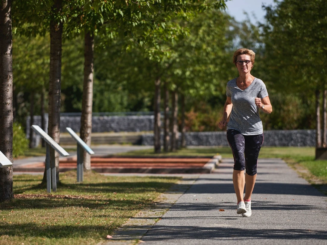 Generationenpark Eine Frau joggt auf einem von Bäumen gesäumten Weg im Generationenpark bei sonnigem Wetter.