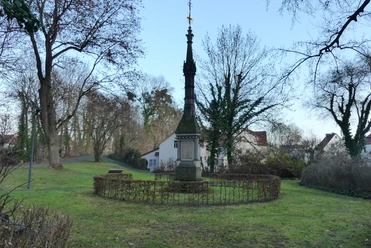 Mühlenwall_Denkmal an Krieg 1870/71 Steinernes Kriegsdenkmal mit Spitze im Park, umgeben von Hecken und Bäumen am Mühlenwall Einbeck.