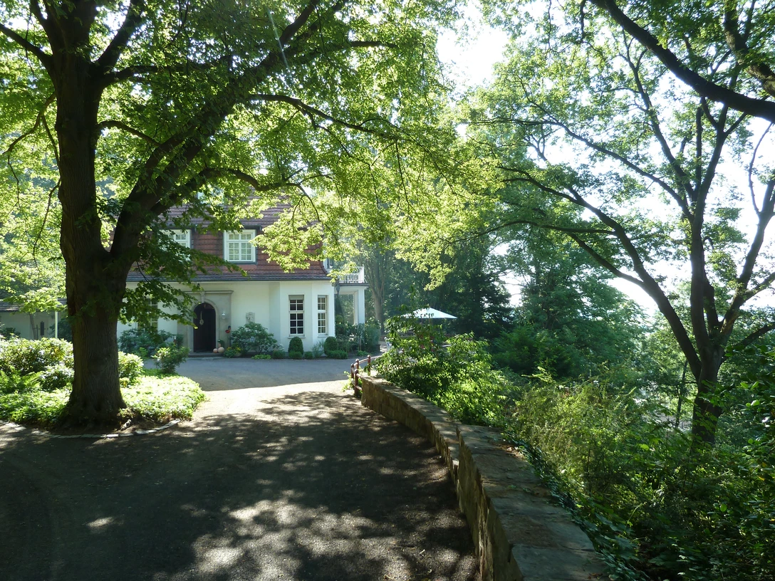 Ringwallanlage und Haus Hünenburg in Achim-Baden Haus Hünenburg in Achim-Baden, umgeben von grünen Bäumen, lässt Sonnenlicht durch das Laub scheinen.