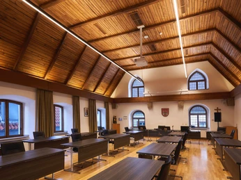 Sitzungssaal Moderner Sitzungssaal mit Holzdach, großen Fenstern, zentralem Tisch und Stühlen in Reihen.