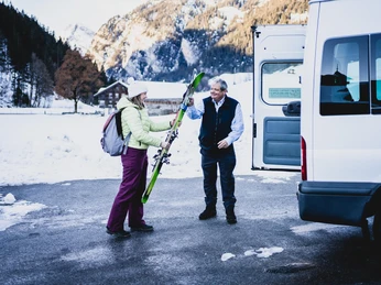 Aide au chargement des skis dans le bus de la tournée des neiges Der Buschauffeur hilft der Frau die Skis in den Schneetourenbus zu ladenThe bus driver helps the woman load the skis into the snow tour busLe chauffeur de bus aide la femme à charger les skis dans le bus de la tournée.