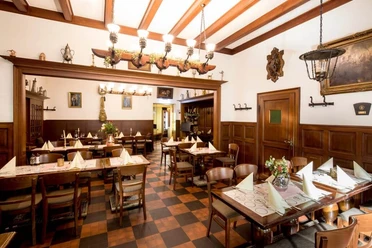 Rustikal eingerichtetes Restaurant mit Holzbalken an der Decke und Bilder in goldenen Rahmen an den Wänden