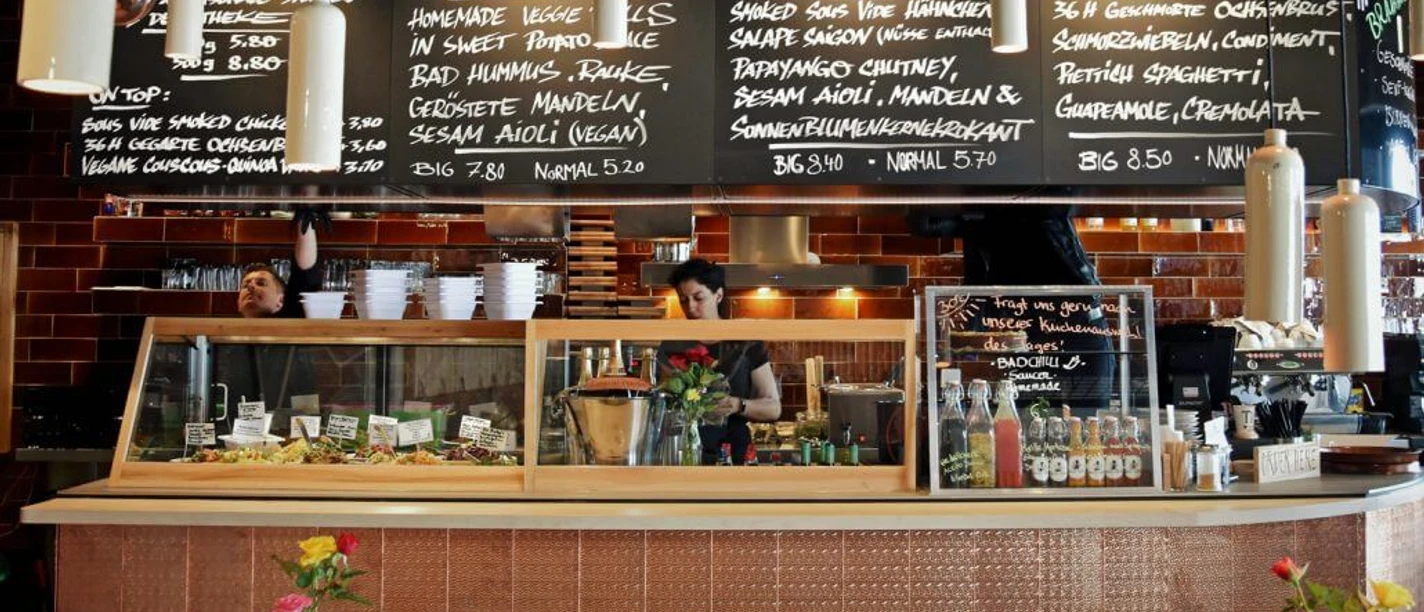 Bad Ape Theke Gekachelte Theke im Bistro. Von der Decke hängen Kreidetafeln mit dem aktuellem Menü.