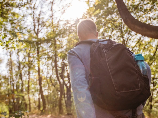 Wandern Ein Wanderer mit Rucksack und Karte spaziert entlang eines Waldpfades im Sonnenlicht.