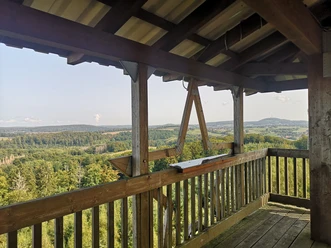 Holzverkleideter Aussichtsturm mit Blick auf bewaldete Hügel und langgezogene, sanfte Täler.