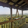 Holzverkleideter Aussichtsturm mit Blick auf bewaldete Hügel und langgezogene, sanfte Täler.