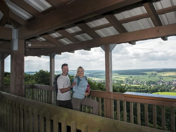 Auf dem Hungerbergturm Ein Paar genießt die weite Aussicht vom überdachten Holz-Aussichtsturm auf weite, grüne Landschaften.