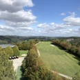 Förderturm Lüderich Weitläufige Golfanlage in grüner Hügellandschaft unter blauem Himmel mit weißen Wolken.