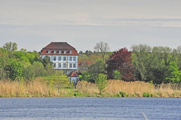 Herrenhaus von Bäumen umgeben, mit Ziegelsteindach und Seeblick, lädt zum Entdecken ein.