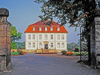 Herrenhaus aus dem 18. Jahrhundert mit rotem Dach, umgeben von Bäumen und einem gepflasterten Weg.