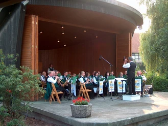 Musikmuschel am Parkplatz Eine Blaskapelle in traditioneller Tracht musiziert in einer überdachten Freiluftbühne.