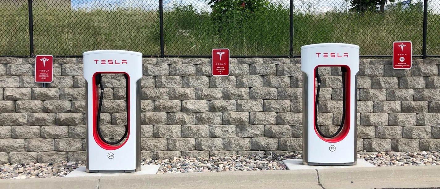 pexels-chad-russell-.JPG Das Bild zeigt zwei Tesla-Ladestationen vor einer Mauer mit Begrünung und klarer Himmel im Hintergrund.