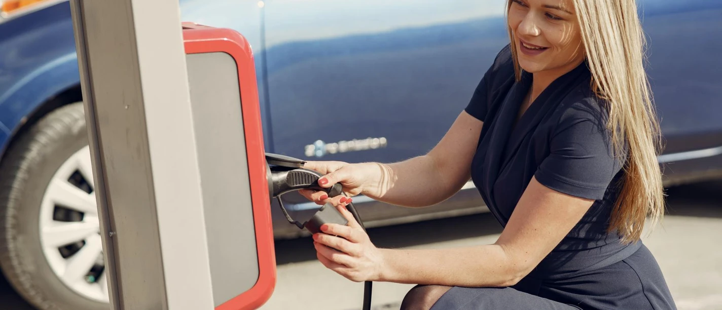 beispiel-e-mobilitaet_pexels-gustavo-fring.JPG Eine Frau kniet lächelnd an einer Ladestation und verbindet ein Elektroauto mit Strom.
