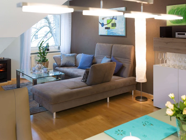 fewo-startpunkt1-wohnzimmer1.jpg Gemütliches Wohnzimmer mit grauem Sofa, Glastisch, modernen Kunstwerken und elegantem Dekor.