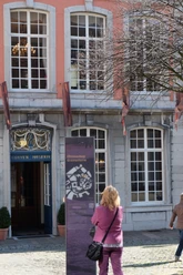 Fassade des Couven Museums. Eine Person betrachtet ein Informationsdisplay vor dem Eingang. Das Gebäude besticht durch große Fenster und eine orangefarbene Fassade.