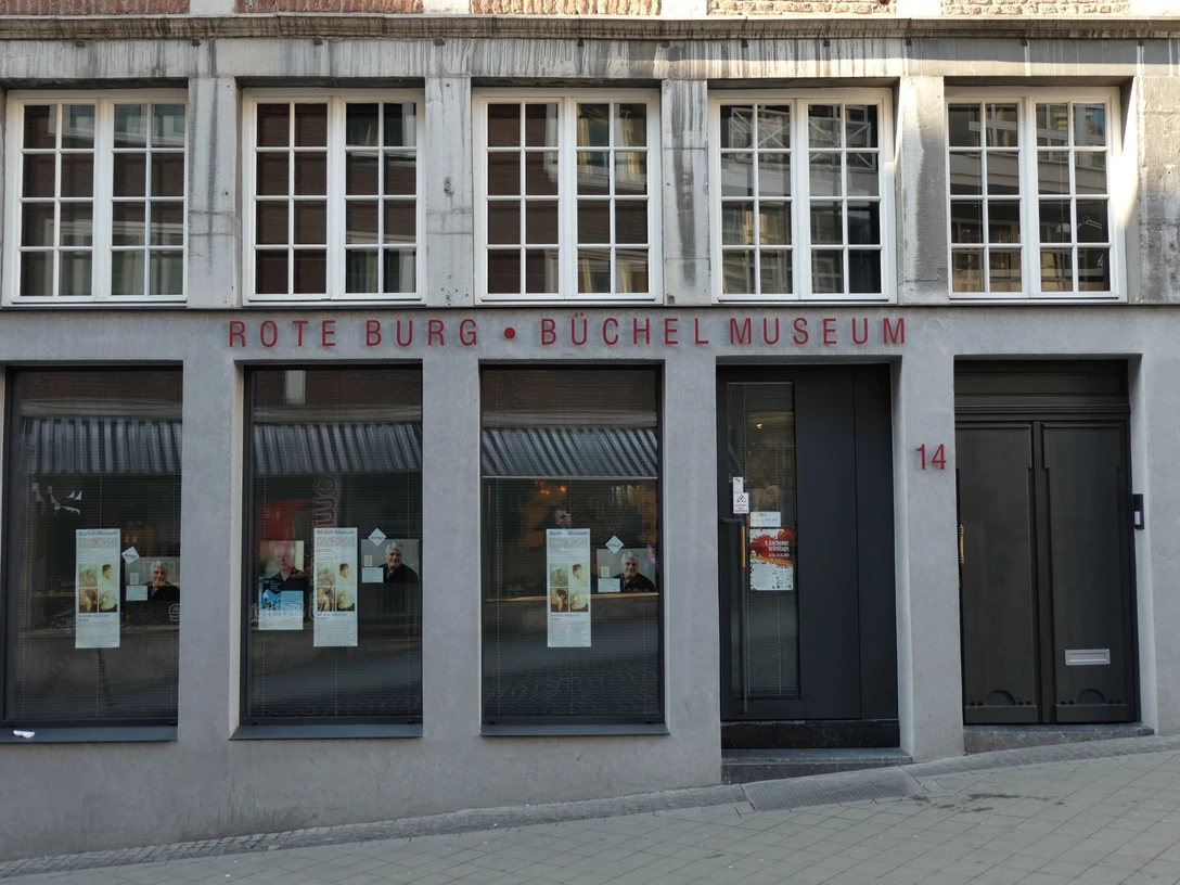 Die Außenansicht des Büchel-Museums zeigt eine graue Fassade mit großen Fenstern und der Aufschrift "Rote Burg - Büchel Museum".