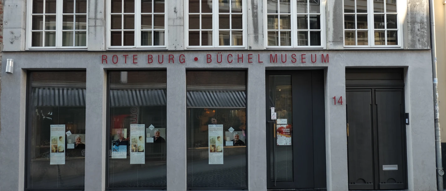 Die Außenansicht des Büchel-Museums zeigt eine graue Fassade mit großen Fenstern und der Aufschrift "Rote Burg - Büchel Museum".