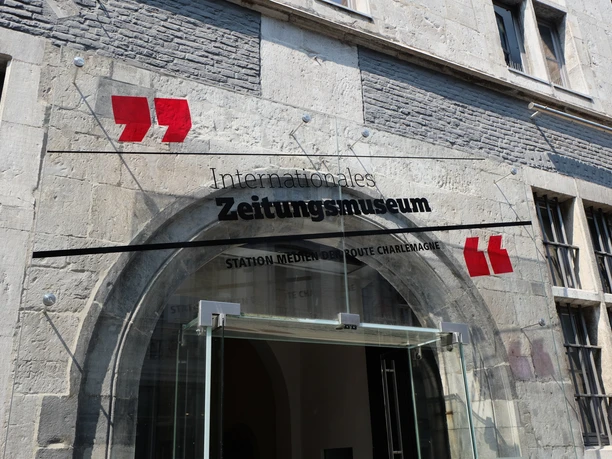 Der Eingang des Internationalen Zeitungsmuseums zeigt ein Glasschild mit dem Schriftzug des Museums.