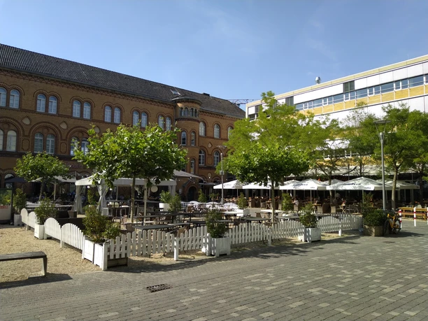 Kapuzinerkarree im Sommer Innenhof eines Gebäudekomplexes mit Außengastronomie und Bäumen unter blauem Himmel.