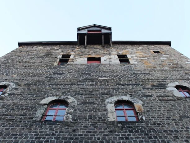 Marschiertor Detailansicht Ein Blick von unten nach oben an einer steinernen Fassade mit roten Fenstern entlang.