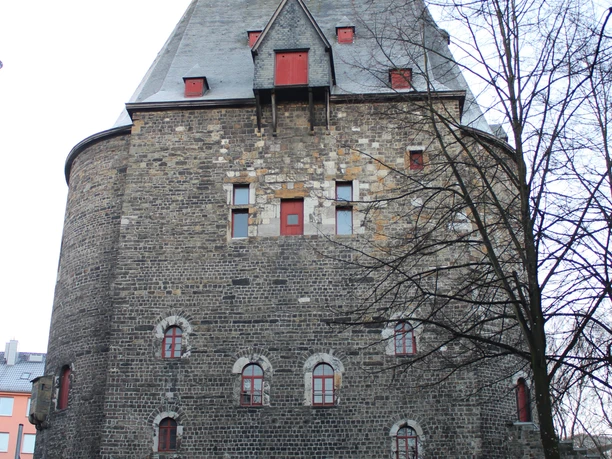 Mittelalterliches Torgebäude mit roten Fenstern im Winter, umgeben von kahlen Bäumen.