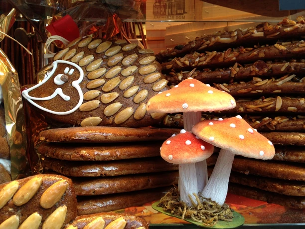 Nobis Printe Igel mit Pilz Ein Lebkuchenigel, reich verziert mit Mandeln, steht vor einer Gruppe leuchtender Fliegenpilze aus Dekormaterial.