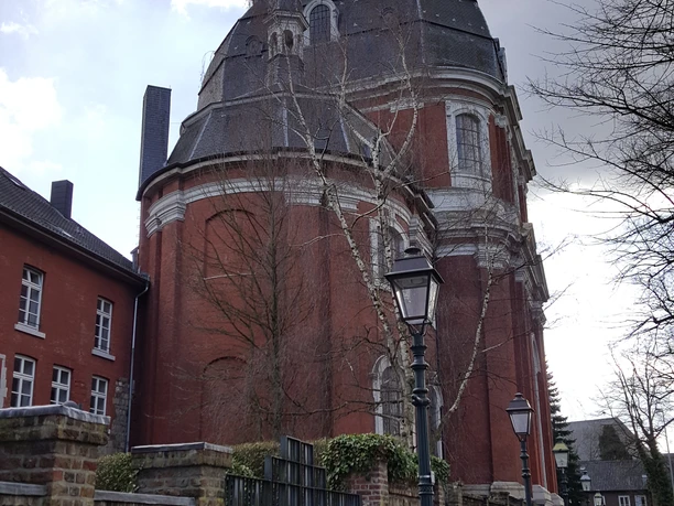 St. Johann Baptist Barocke Kirche mit rotem Ziegelstein und einer markanten Kuppel hinter einer Steinmauer..