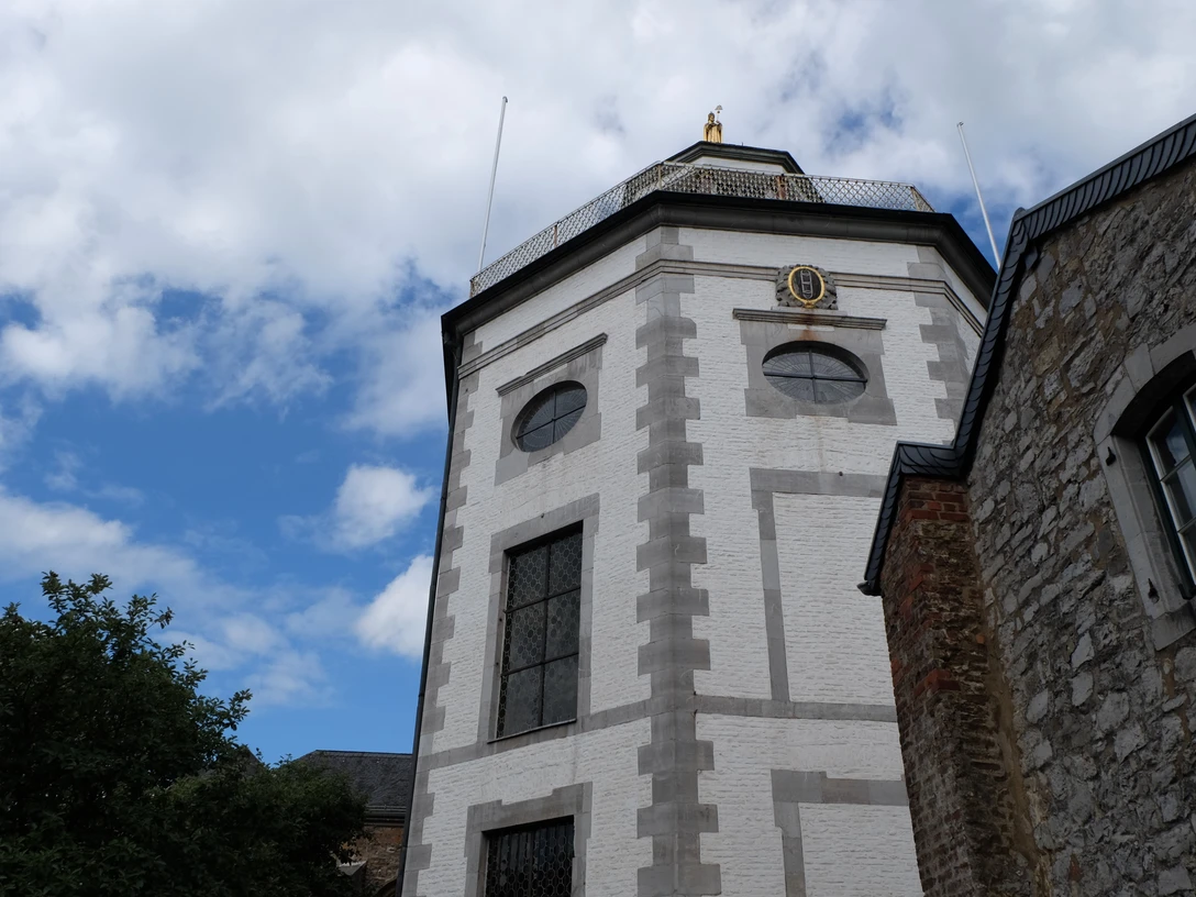 Backsteinturm einer Kirche mit achteckigem Aufbau, umgeben von Bäumen vor leicht bewölktem Himmel.
