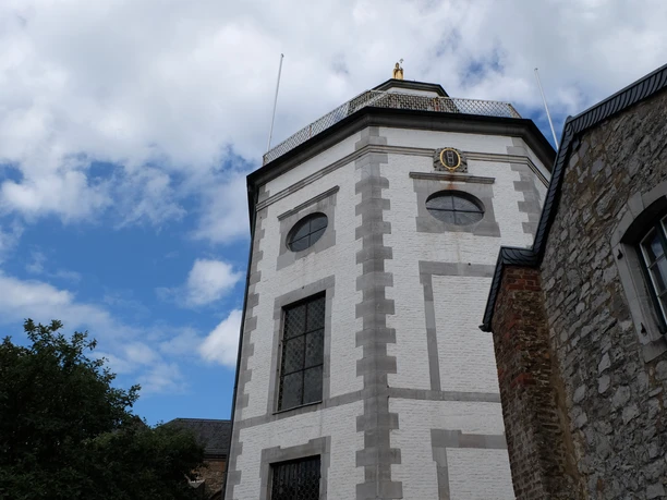 St. Kornelius Backsteinturm einer Kirche mit achteckigem Aufbau, umgeben von Bäumen vor leicht bewölktem Himmel.