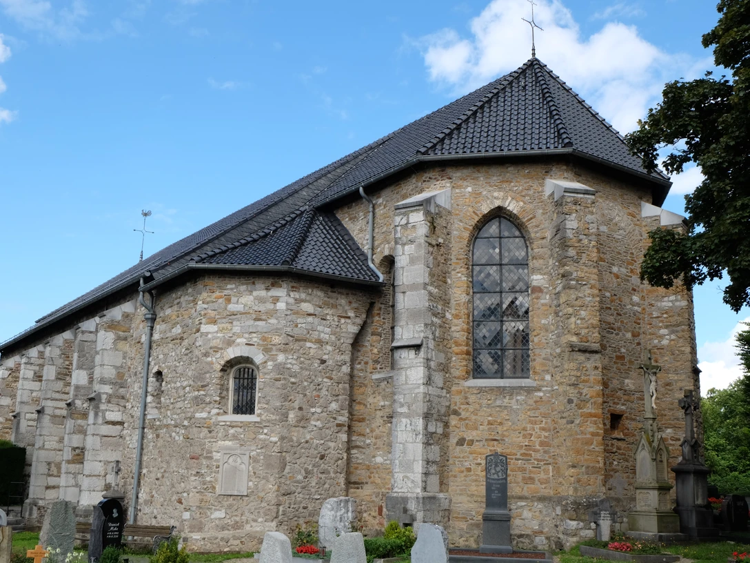 Kirche aus hellbraunen Steinen vor einer Grabesstätte unter blauem Himmel.