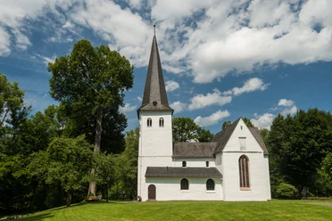 Bonte Kerke Wiedenest Eine idyllische Kirche mit Spitzdach, umgeben von grünen Bäumen, unter blauem Himmel.