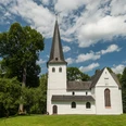 Bonte Kerke Wiedenest Eine idyllische Kirche mit Spitzdach, umgeben von grünen Bäumen, unter blauem Himmel.