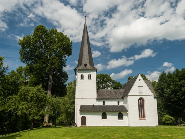 Bonte Kerke Wiedenest Eine idyllische Kirche mit Spitzdach, umgeben von grünen Bäumen, unter blauem Himmel.