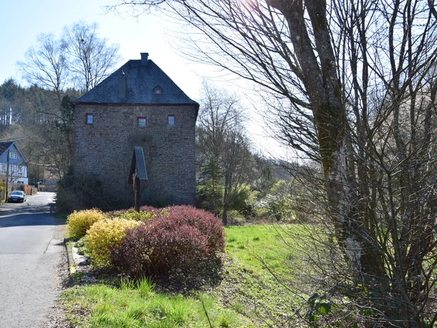 Burghaus Volperhausen Steinernes Fachwerkhaus in ländlicher Umgebung mit Bäumen und blühenden Sträuchern an einem sonnigen Tag.