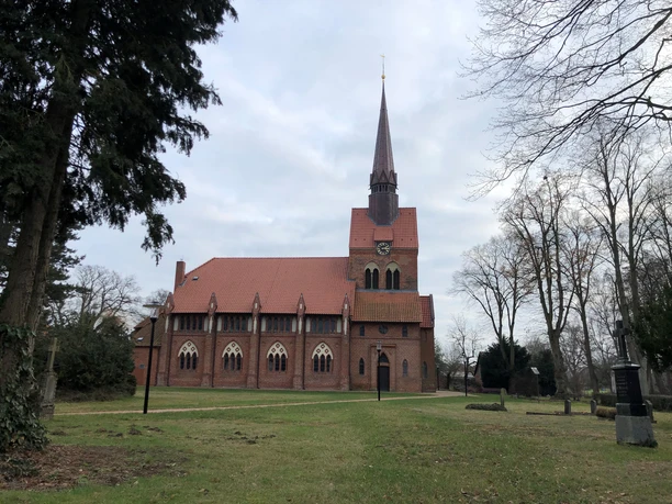 Backsteinkirche St. Michaelis in Heemsen, umgeben von Bäumen auf einer großen, offenen Grünfläche.