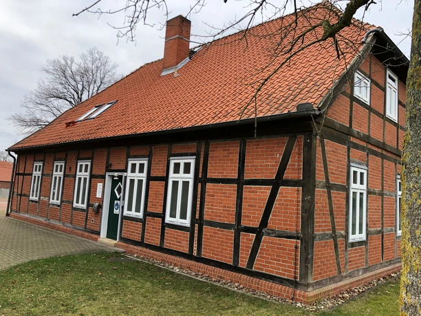 Küsterhaus Rotes Fachwerkhaus mit weißen Fenstern und rotem Ziegeldach, barrierefreier Eingang seitlich.