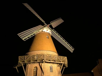 A historic windmill with an illuminated winged cross against a dark night sky.