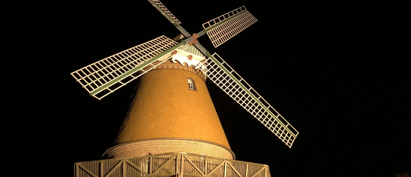 Hochzeitsmühle Landesbergen A historic windmill with an illuminated winged cross against a dark night sky.