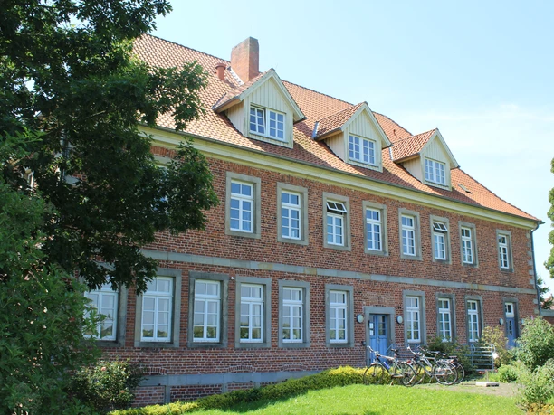 Amtshaus Westen Historisches Gebäude mit roter Backsteinfassade, hohem Dach und zahlreichen Fenstern umgeben von Bäumen.