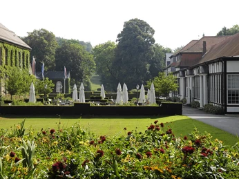 Gräflicher Park Historische Parkanlage mit gepflegten Blumenbeeten, Sonnenschirmen und umrahmt von eleganten Gebäuden.