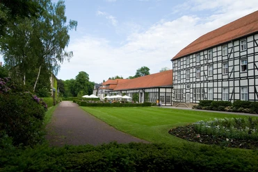 image Fachwerkgebäude mit roten Dächern neben einem gepflegten Garten mit Rasenfläche und Gehweg.