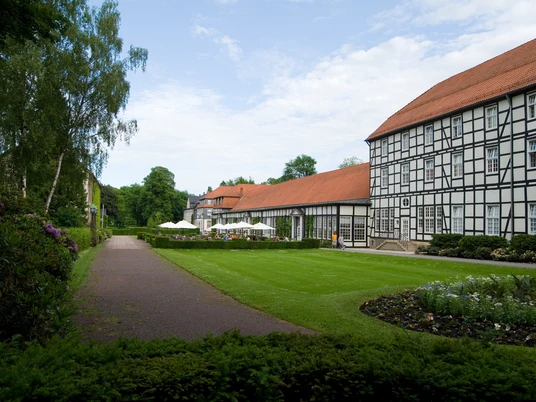 image Fachwerkgebäude mit roten Dächern neben einem gepflegten Garten mit Rasenfläche und Gehweg.