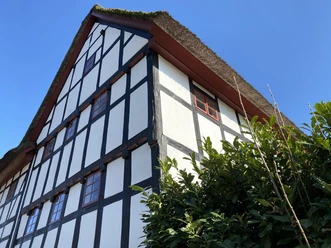 Das "Weiße Pferdchen" in Hohkeppel Fachwerkhaus mit Strohdach vor blauem Himmel, umgeben von grünen Büschen in Lindlar.