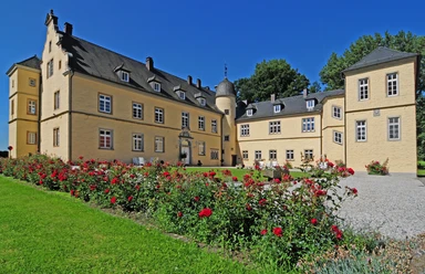 Das Bild zeigt Schloss Crollage mit blühenden Rosen im Vordergrund, umgeben von einem blauen Himmel.