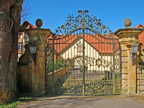 Hoftor von Schoss Crollage Prächtiges schmiedeeisernes Tor mit kunstvollen Verzierungen vor dem Schloss Crollage im Sonnenschein.