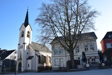 Ev. Kirche Am Markt <p>Weiße Kirche neben Altbau und Baum, blauer Himmel, in Wipperfürth. Hauptstraße im Vordergrund.</p>