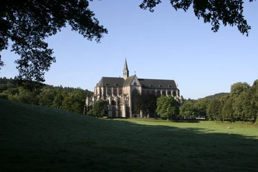 Altenberger Dom Nordansicht Die Abtei Altenberg im Morgenlicht, umgeben von Wiesen und Bäumen unter einem klaren blauen Himmel.