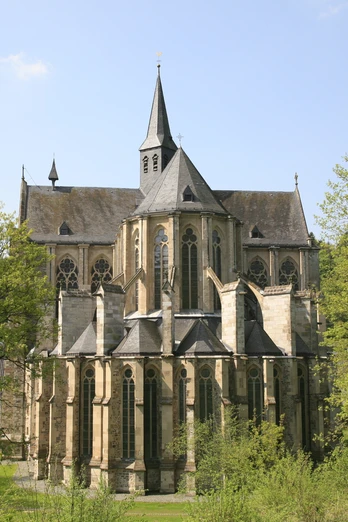 Ostchor Altenberger Dom Gotische Kirche umgeben von grünem Park mit blühenden Bäumen, blauer Himmel im Hintergrund.